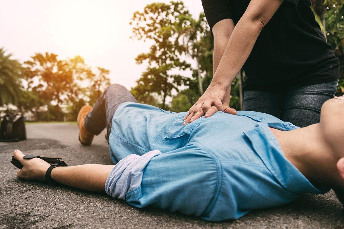 Person performing CPR on an individual lying on the ground in an outdoor setting.