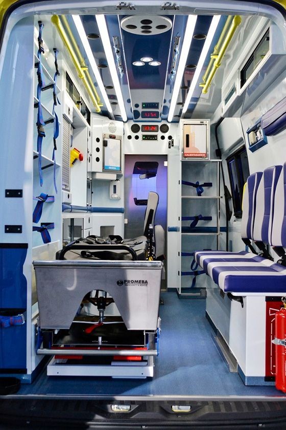 Interior view of an ambulance with medical equipment, stretcher, seats, and emergency supplies.